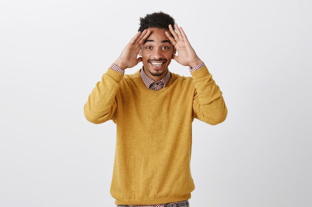 Guy n'avait pas prévu de voir un ami de longue date à la fête du B-Day. Heureux étudiant masculin à la peau sombre avec une coiffure afro tenant les paumes sur le front et souriant largement, étant agréablement surpris