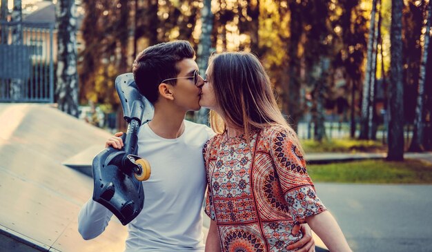 Guy avec planche à roulettes embrassant sa petite amie. journée ensoleillée