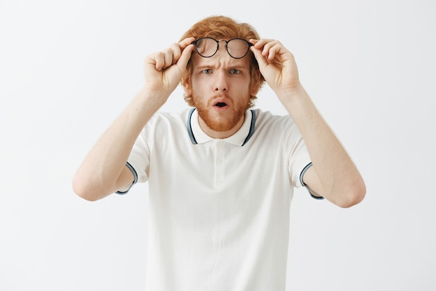 Guy rousse barbu confus posant contre le mur blanc avec des lunettes