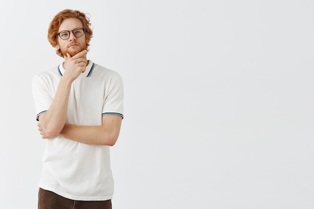 Guy rousse barbu réfléchie posant contre le mur blanc avec des lunettes