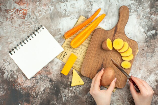 Hacher à la main divers légumes et deux types de couteau à fromage sur une planche à découper en bois sur un vieux journal