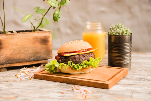 Hamburger avec de la laitue et du fromage sur une planche en bois avec une bouteille de jus sur la table