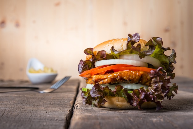 Hamburger de poulet fait maison avec des frites, de la laitue, de la tomate et de l&#39;oignon sur une planche en bois.