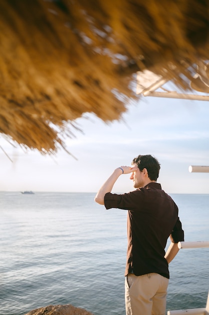 Hansome homme debout et regardant loin en bord de mer en chemise noire pendant la journée.
