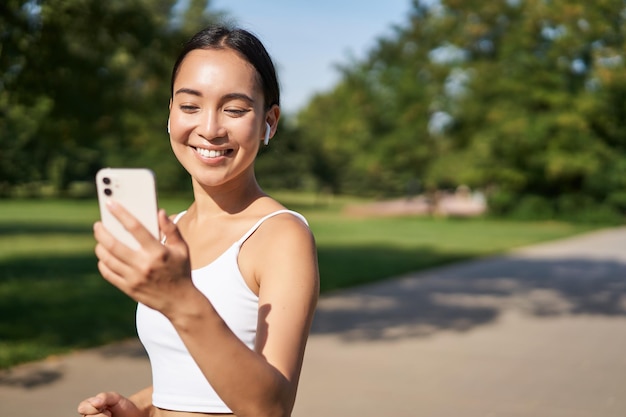 Happy asian fitness girl courir et vérifier ses objectifs quotidiens de statistiques sur l'application pour smartphone jeune femme jo