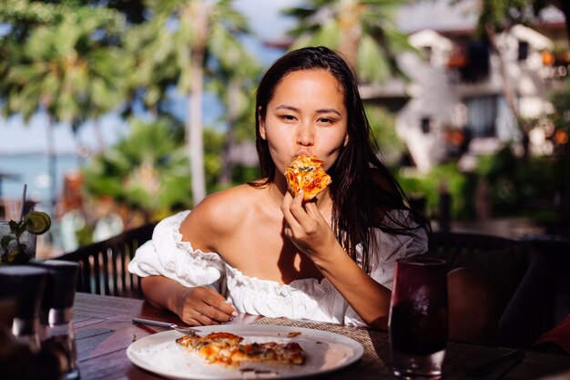 Happy Asian jolie femme faim ayant une pizza à la lumière du coucher du soleil journée ensoleillée dans le restaurant en plein air Femme appréciant la nourriture s'amuser au déjeuner