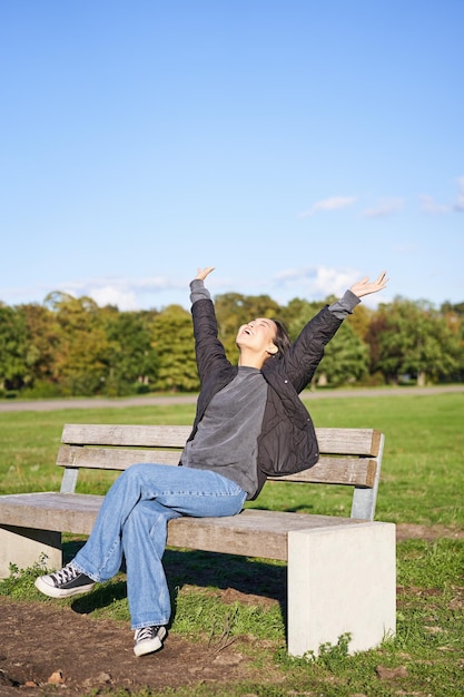 Photo gratuite happy asian woman stretching her hands sitting on bench avec visage excité souriant sentiment de plaisir fr