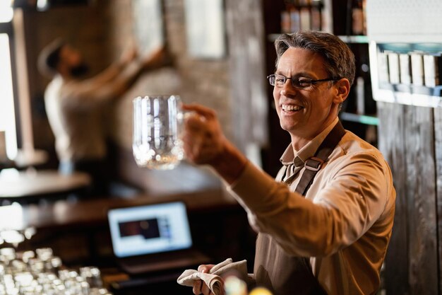 Happy mid adult barista nettoyage verre à boire après les heures de travail dans un pub