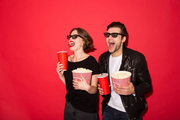 Happy punk couple in eyeglasses holding soda and popcorn