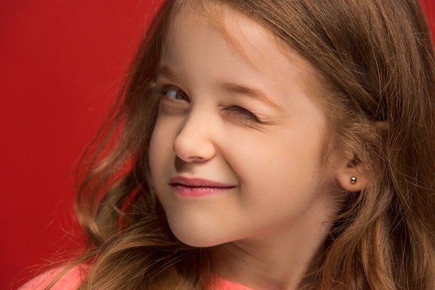 Happy teen girl debout, souriant isolé sur fond de studio rouge à la mode.