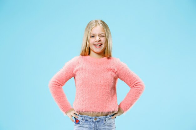 Happy teen girl debout, souriant isolé sur un studio bleu branché.