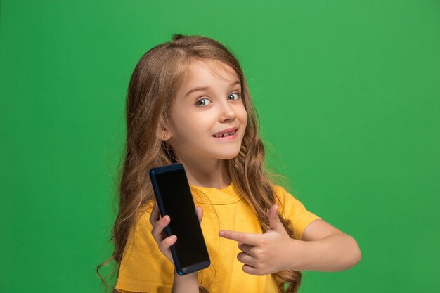 Happy teen girl debout, souriant avec un téléphone mobile sur fond de studio vert branché. Beau portrait de femme en demi-longueur. Émotions humaines, concept d'expression faciale.