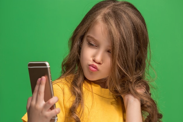 Happy teen girl debout, souriant avec un téléphone mobile sur studio vert branché