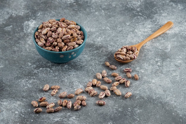 Haricots crus et cuillère en bois sur marbre.