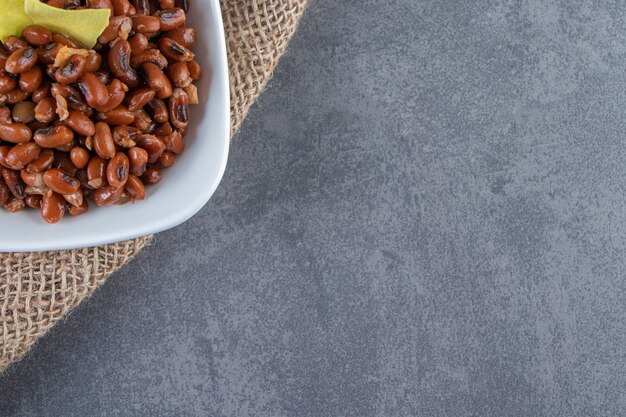 Haricots crus et feuilles de lasagne dans un bol sur la serviette en toile de jute, sur le fond bleu.