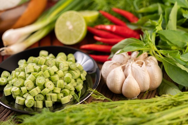 Les haricots longs, l'ail, le piment, le citron vert, l'oignon vert et le cha-om sont placés sur une table en bois