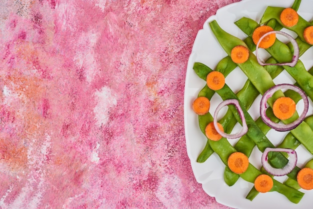 Haricots verts et carottes dans une assiette blanche.