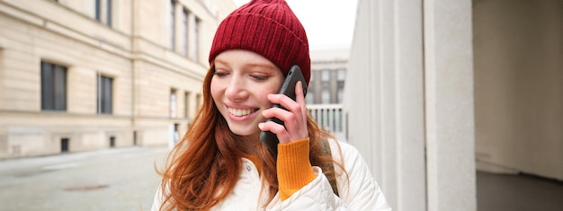 Photo gratuite haut débit mobile et personnes souriantes, une jeune femme rousse se promène en ville et parle au téléphone portable