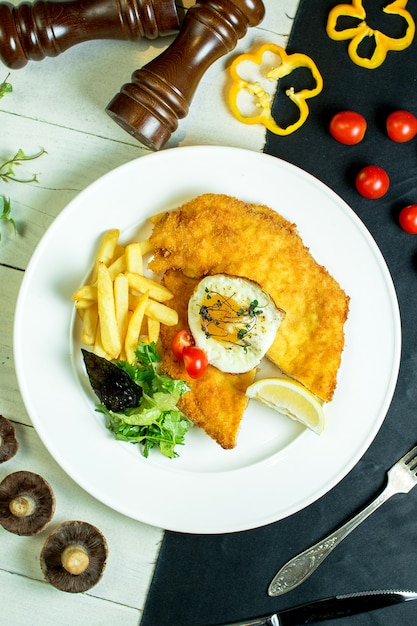 haut de filet de poulet pané servi avec des frites oeuf au plat et tomates cerises sur la plaque