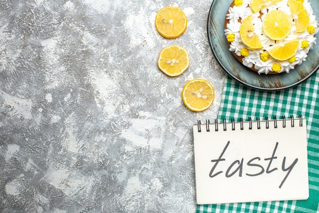 Haut de la moitié du gâteau avec crème blanche et tranches de citron sur un plateau sur une nappe à carreaux blanc vert. savoureux écrit sur ordinateur portable