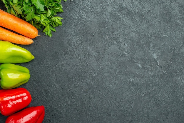 Haut de la page vue rapprochée des carottes vertes et des poivrons sur le côté gauche sur la table gris foncé