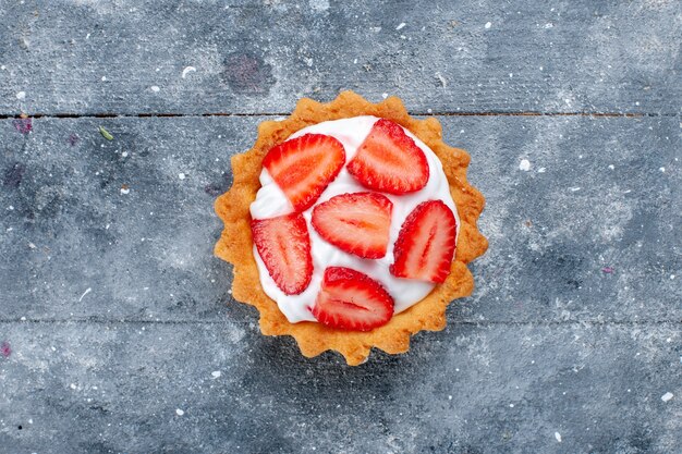 Photo gratuite haut de la page vue rapprochée du petit gâteau crémeux avec des fraises en tranches sur un bureau gris