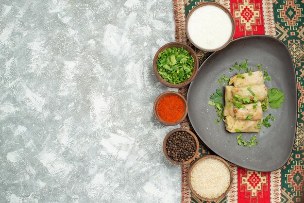 Haut de la page vue rapprochée avec des herbes assiette de chou farci et bols d'herbes papper noir épices riz et crème sure sur nappe colorée avec des motifs sur le côté droit de la table