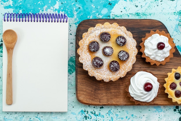 Haut de la page vue rapprochée de petits gâteaux aux fruits et crème alogn avec bloc-notes sur bleu clair cuire au four la couleur du gâteau au sucre sucré