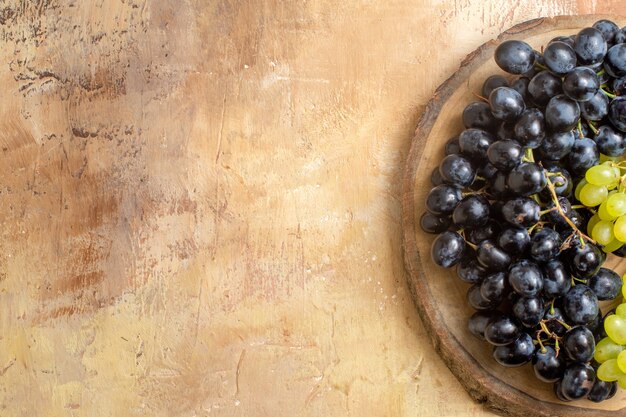 Haut de la page vue rapprochée de la planche de bois de raisins avec des raisins verts et noirs sur la table crème