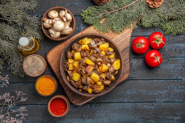 Haut de page vue rapprochée plat et légumes assiette de pommes de terre aux champignons sur planche de bois à côté de trois tomates et épices colorées sous huile dans des branches d'arbres en bouteille et bol de champignons
