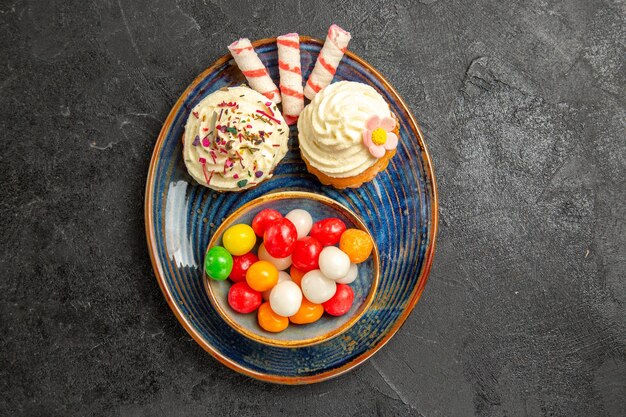 Haut vue en gros plan des bonbons sur l'assiette les appétissants cupcakes à côté du bol de bonbons colorés sur la table sombre