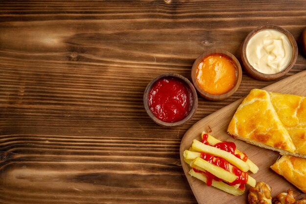 Haut vue en gros plan poulet et sauces tarte au poulet frites avec ketchup sur la planche de bois à côté des bols d'épices et de sauces colorées