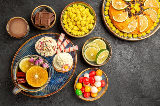 Haut vue rapprochée des bonbons sur l'assiette les cupcakes appétissants une tasse de gâteau aux tisanes à l'orange et des bols de bonbons au chocolat au citron vert et de la crème au chocolat sur la table