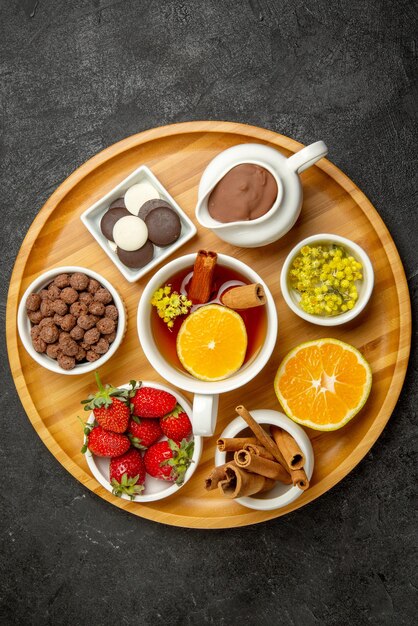 Haut vue rapprochée des bonbons sur une assiette de table de fraises au chocolat, de bâtons de cannelle au citron et d'une tasse de thé au citron