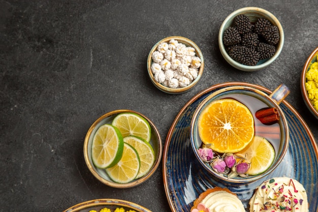 Haut vue rapprochée bonbons sur la table bols de baies sucrées agrumes bonbons blancs et les cupcakes et une tasse de thé au citron et cannelle sur la table sombre