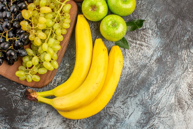 Haut vue rapprochée fruits trois bananes pommes raisins verts et noirs sur la planche de cuisine
