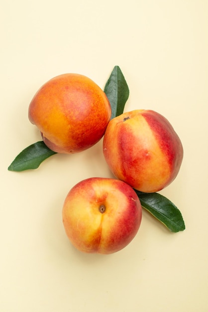 Haut vue rapprochée nectarine trois nectarines avec des feuilles sur la surface blanche