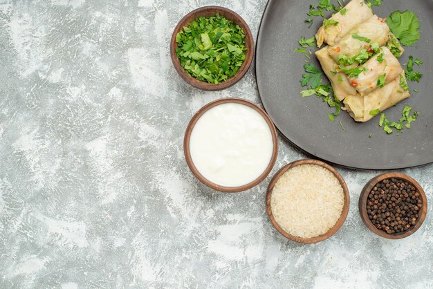 Haut vue rapprochée plat avec assiette d'herbes de chou farci à côté de bols de riz à la crème sure aux herbes et poivre noir sur le côté droit de la table