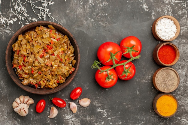 Haut vue rapprochée plat de haricots verts plat de haricots verts et tomates dans l'assiette quatre bols d'épices ail et tomates avec pédicelles sur le tableau noir