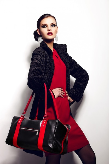 Photo gratuite haute couture look.glamour closeup portrait de belle sexy élégante brune caucasienne jeune femme modèle en robe rouge avec un sac noir maquillage lumineux, avec des lèvres rouges, avec une peau parfaitement propre en studio