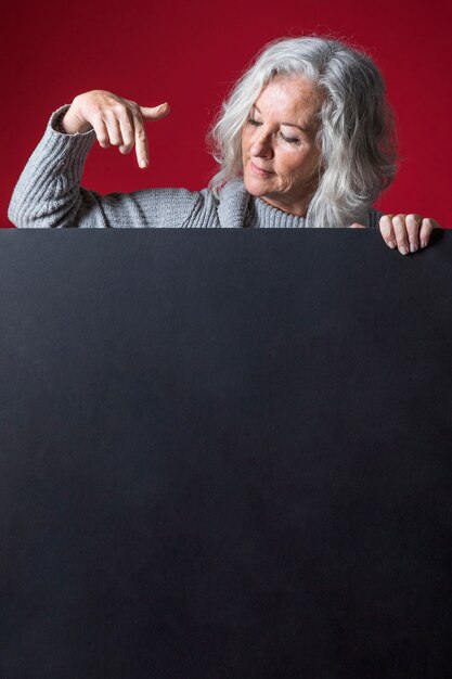 Haute femme pointant son doigt vers le bas sur une pancarte noire vierge sur fond rouge