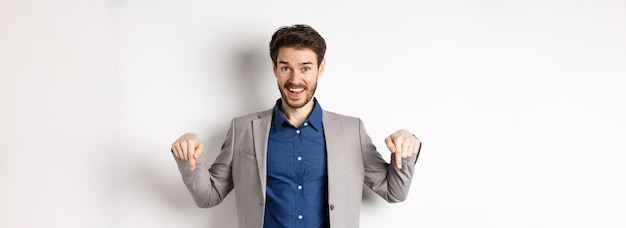 Photo gratuite hé, regardez cet homme d'affaires heureux en costume pointant les doigts vers le bas et souriant invitant à l'événement sho