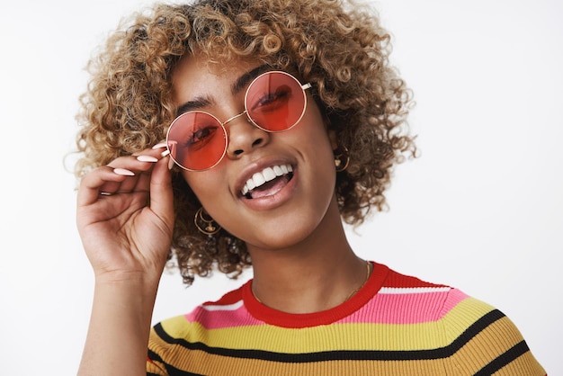 Hé, tu veux t'amuser Portrait d'une fêtarde afro-américaine joyeuse et élégante avec une coupe de cheveux blonde et un nez percé levant la tête dans une pose confiante et froide souriante portant des lunettes de soleil à la mode