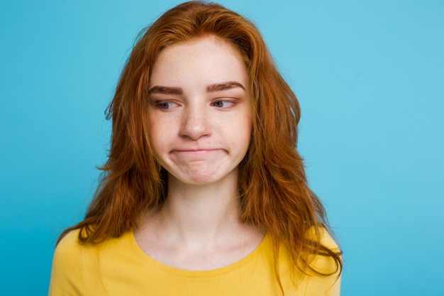 Headshot Portrait d&#39;adolescent roux tendre avec une expression sérieuse en regardant la caméra. Modèle de femme caucasienne avec des cheveux en gingembre posant à l&#39;intérieur. Fond bleu pâtissier. Espace de copie.