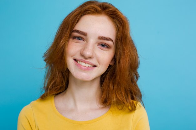Headshot Portrait d&#39;une fille heureuse de gingembre avec des taches de rous souriantes en regardant la caméra. Fond bleu pastel. Espace de copie.