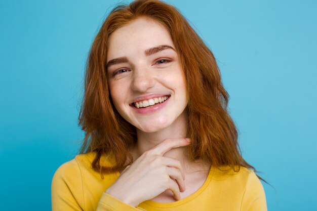 Headshot Portrait d&#39;une fille heureuse de gingembre avec des taches de rous souriantes en regardant la caméra. Fond bleu pastel. Espace de copie.