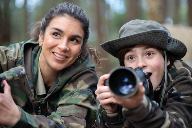 Héhé, prendre des photos en forêt. Mère et fils avec des caméras modernes allongées sur le sol, tenant des caméras, regardant quelque chose. Parentalité, famille, concept de loisirs