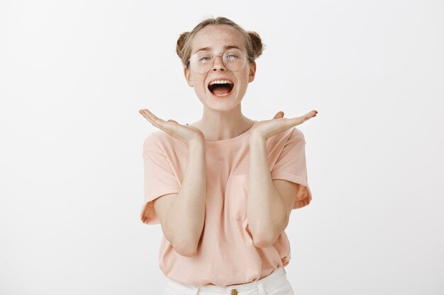 Heureuse adolescente rousse réussie posant contre le mur blanc