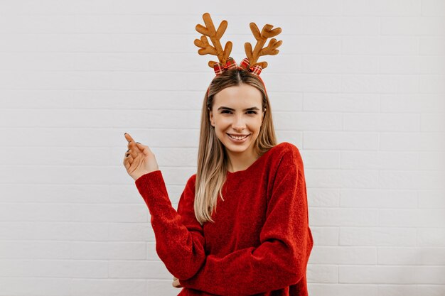 Heureuse adorable dame en pull rouge en coiffures de Noël souriant et regardant la caméra sur fond isolé