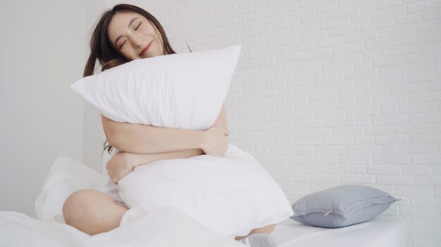 Heureuse belle femme asiatique se réveiller en souriant et en étirant ses bras dans son lit dans la chambre.